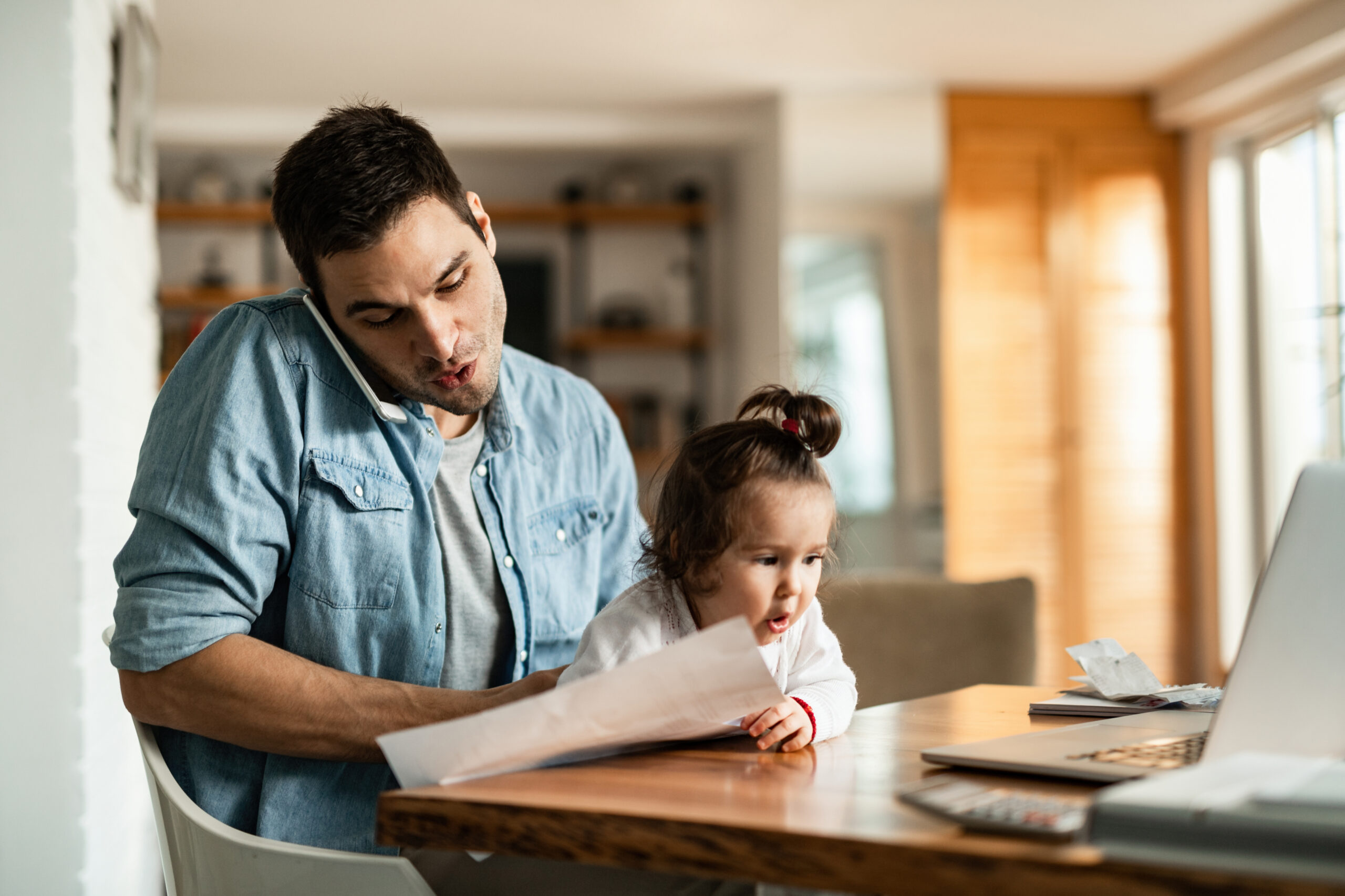 Young Father With Daughter Talking On The Phone While Working At
